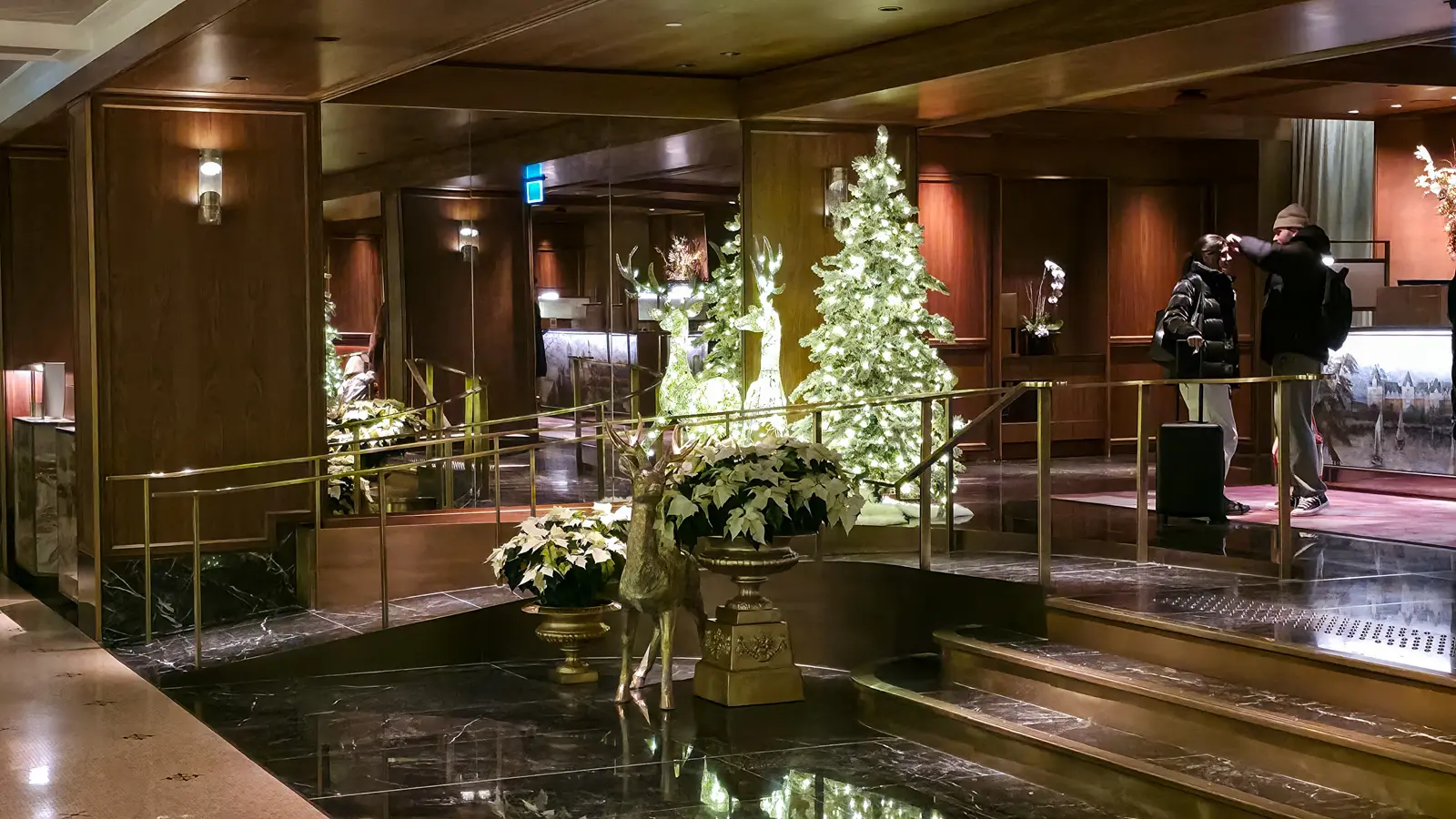 A gold deer and white poinsettias in gold urns near the Fairmont Royal York front desk, with a lit tree behind