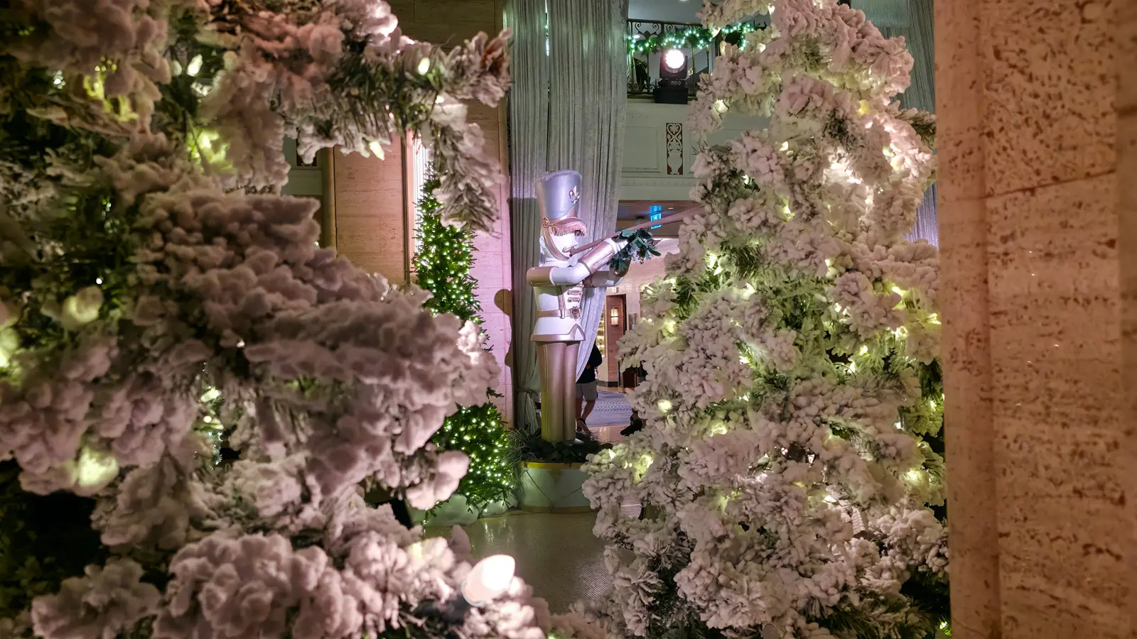 A giant white nutcracker with a trumpet, framed by two snowy, lit Christmas trees in the Fairmont Royal York lobby