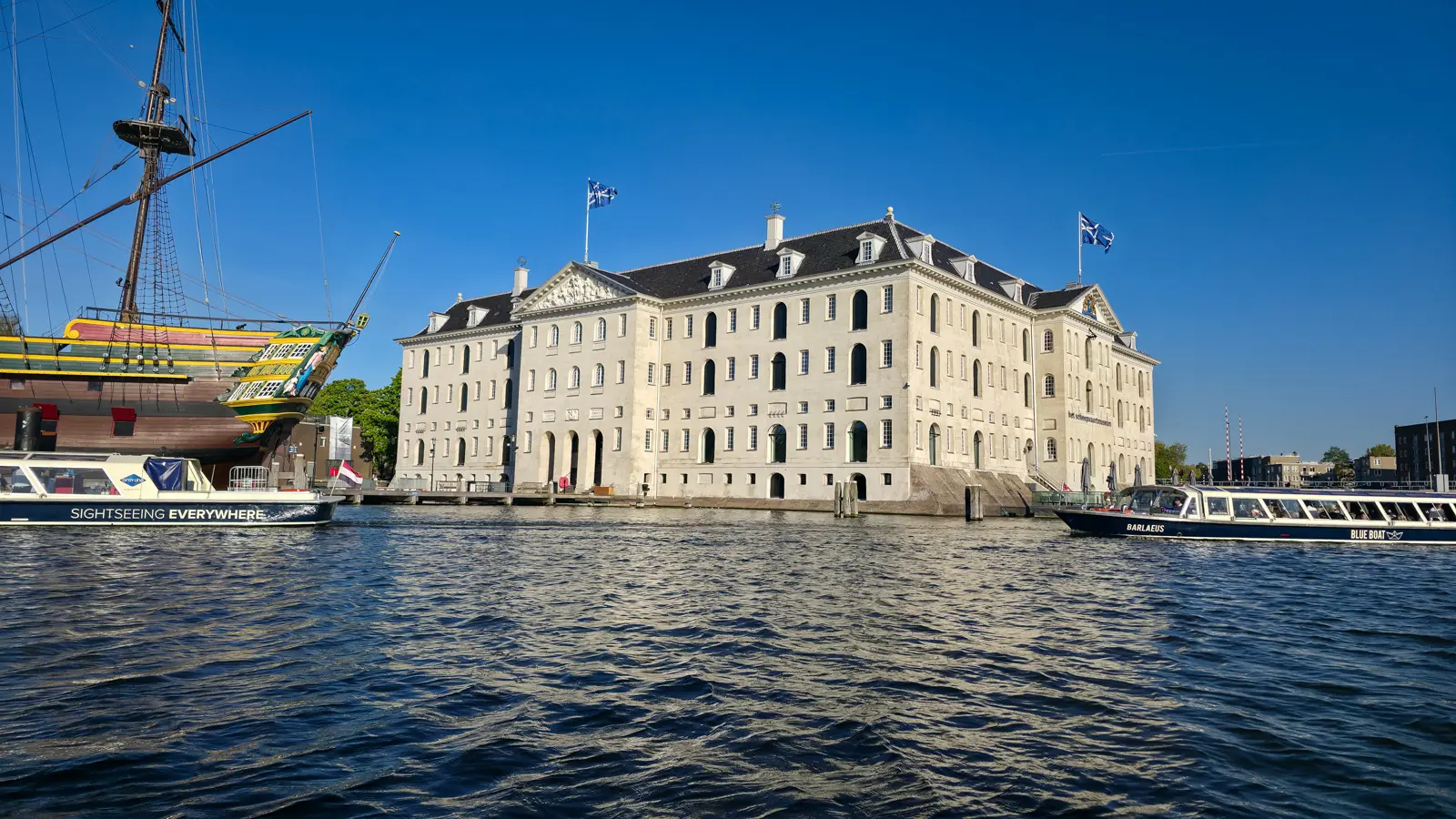 Het Scheepvaartmuseum seen from a canal cruise, a pale stone storehouse with the replica ship Amsterdam moored beside it, Amsterdam