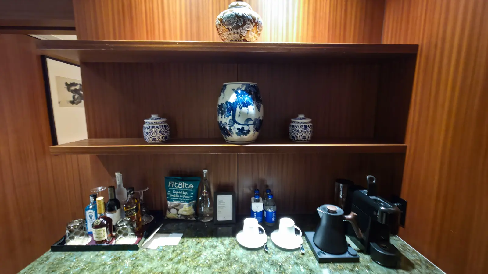 The in-suite bar at Shangri-La Toronto, with blue-and-white porcelain on wooden shelves above spirits, snacks, cups and a kettle