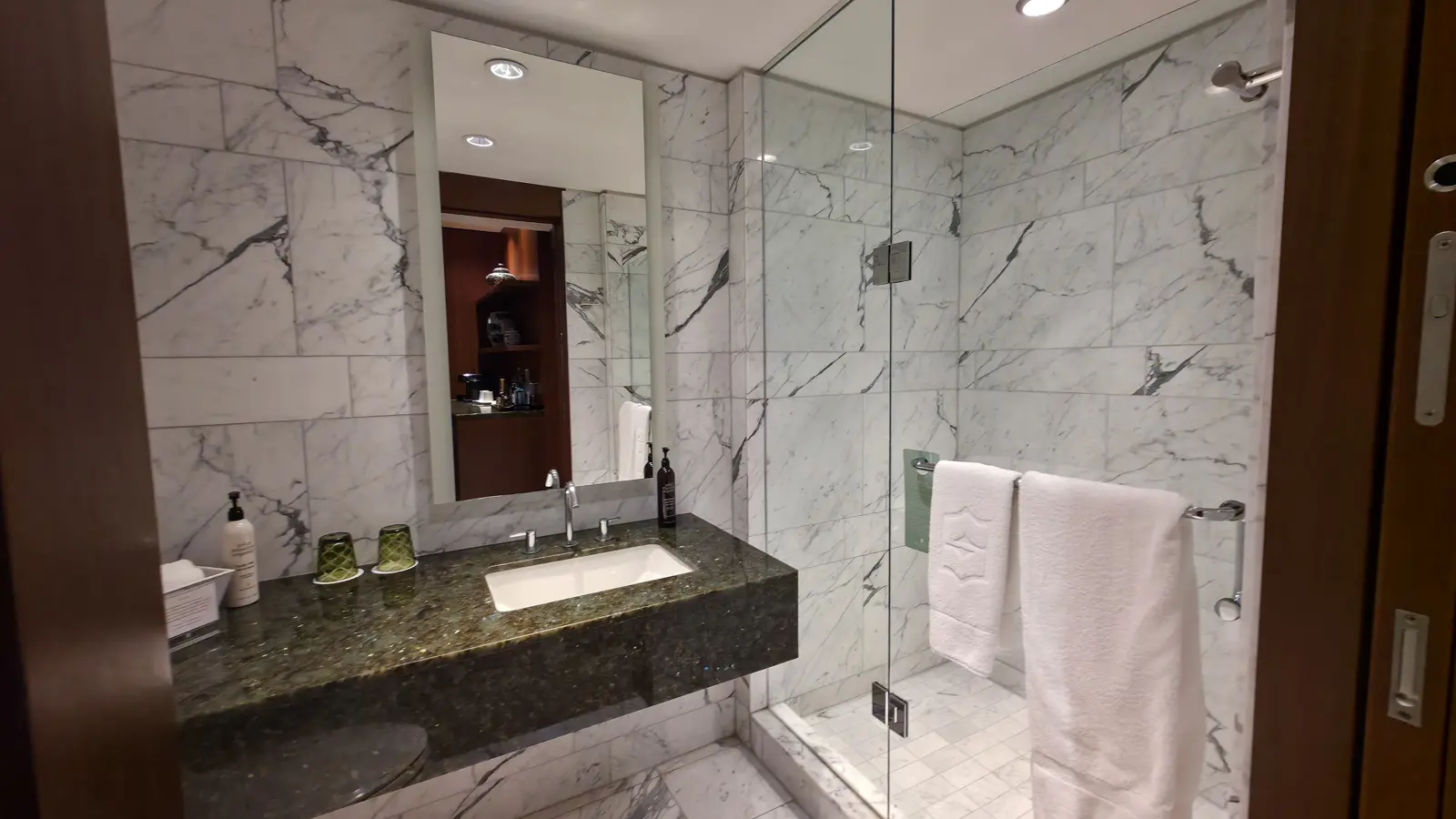 The guest bathroom of a Shangri-La Toronto suite, with a green stone vanity and a walk-in glass shower