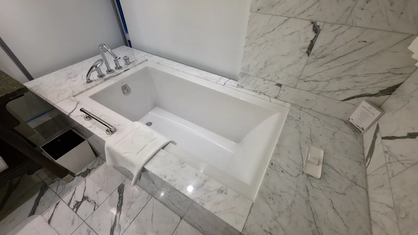 A deep-soaking bathtub set into marble in the master bathroom of a Shangri-La Toronto suite, with a hand shower