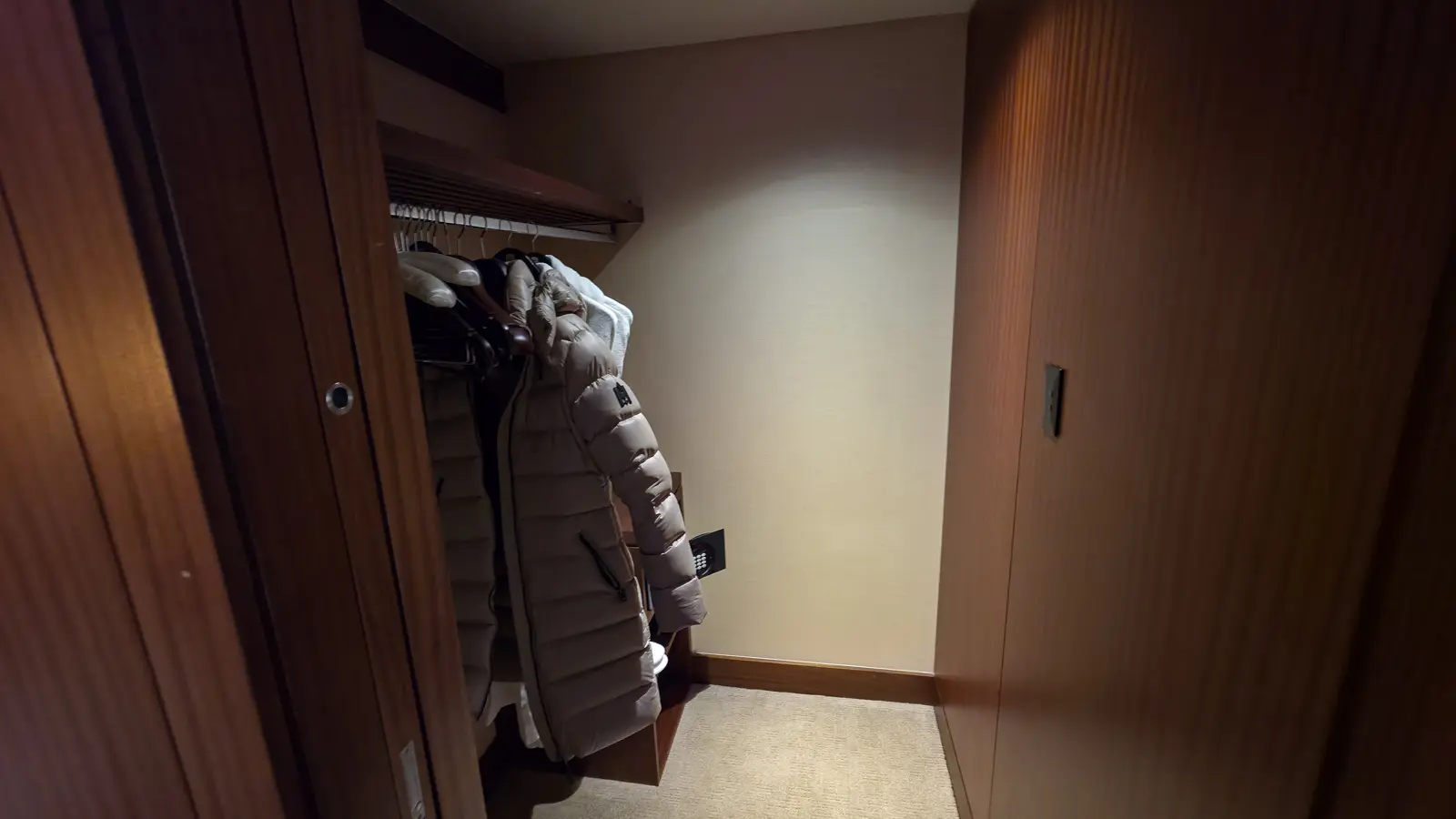 The walk-in wardrobe of a Shangri-La Toronto suite, with a winter coat on wooden hangers and an in-room safe