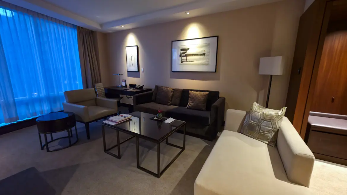 The living room of a Deluxe Suite at Shangri-La Toronto, with a sofa, chaise, armchair, glass coffee table and framed ink art