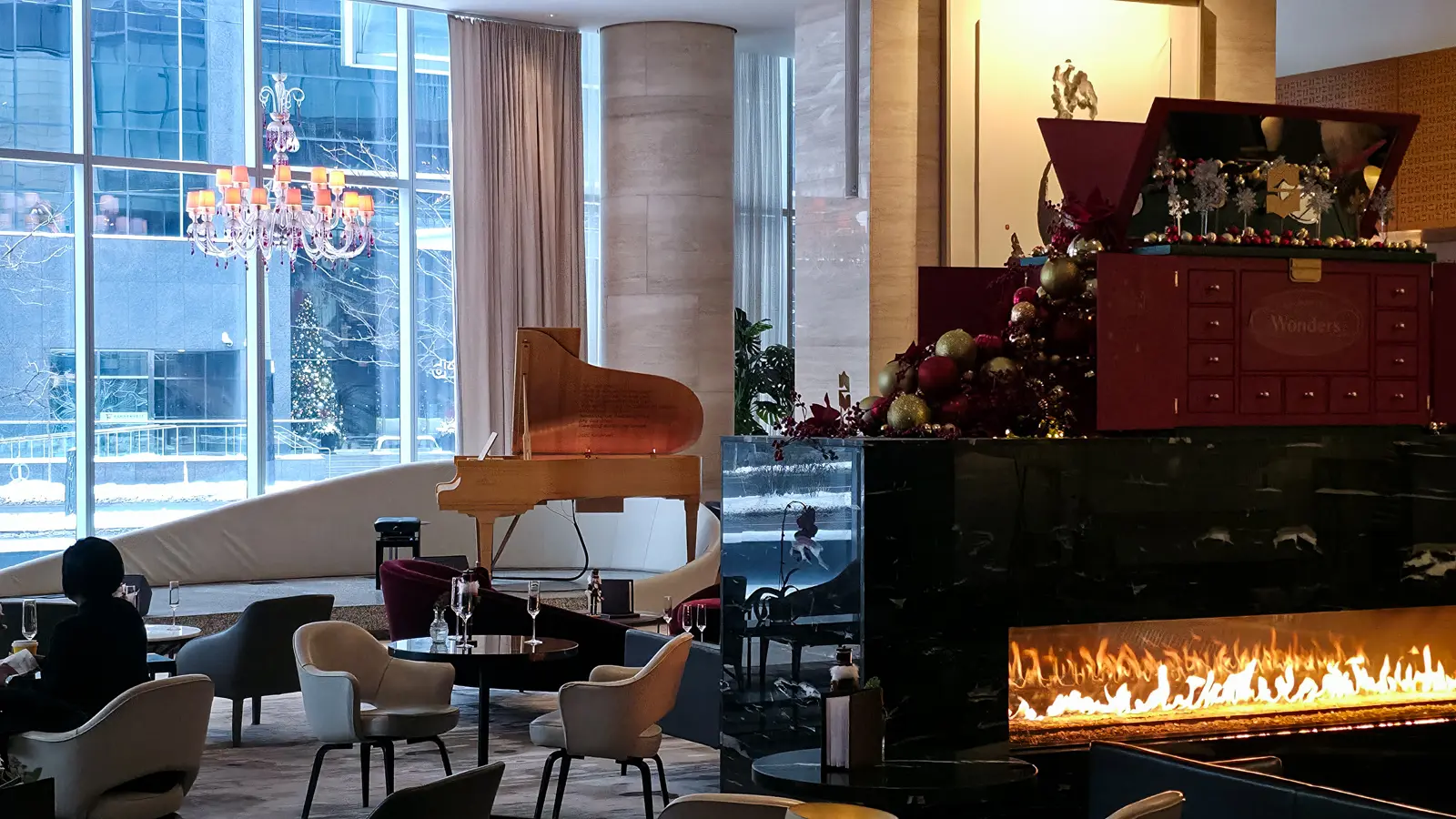 The Shangri-La Toronto Lobby Lounge at Christmas, with a grand piano, chandelier, fireplace and a red Wonders chest of baubles