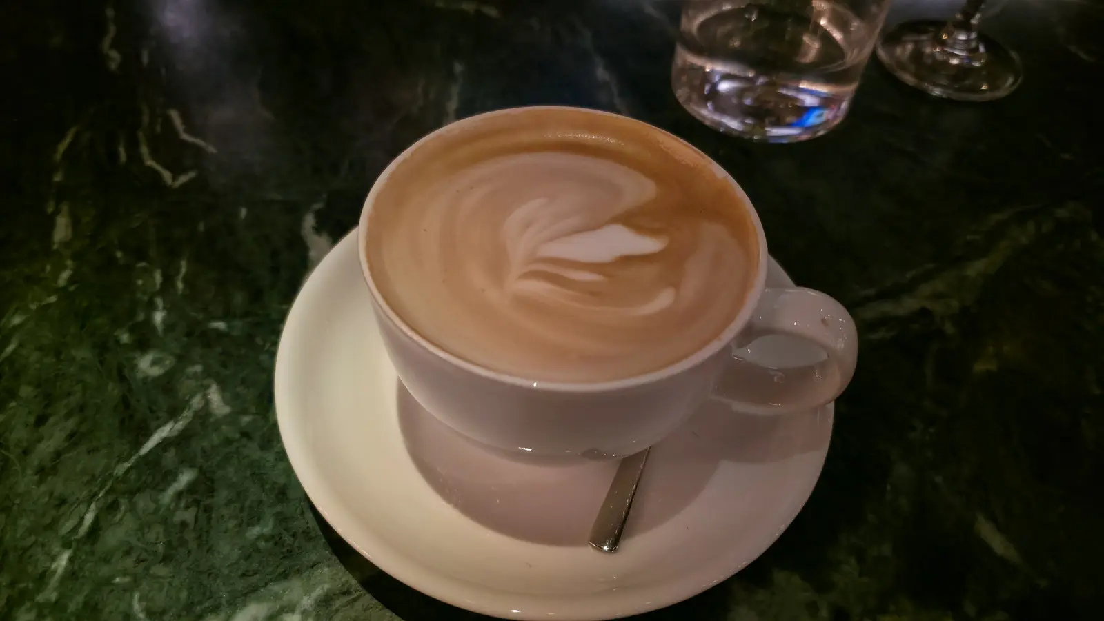 A flat white with latte art in a white cup and saucer on a dark green marble table at The Duchess, Amsterdam