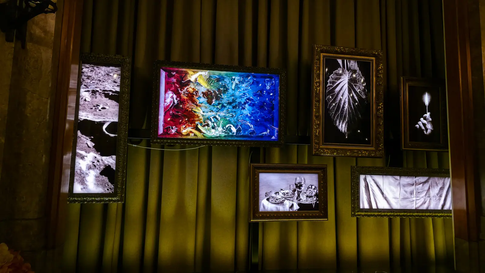 Ornate gilt frames on a curtained wall at The Duchess, glowing with images of the moon, birds, a leaf and a lit match