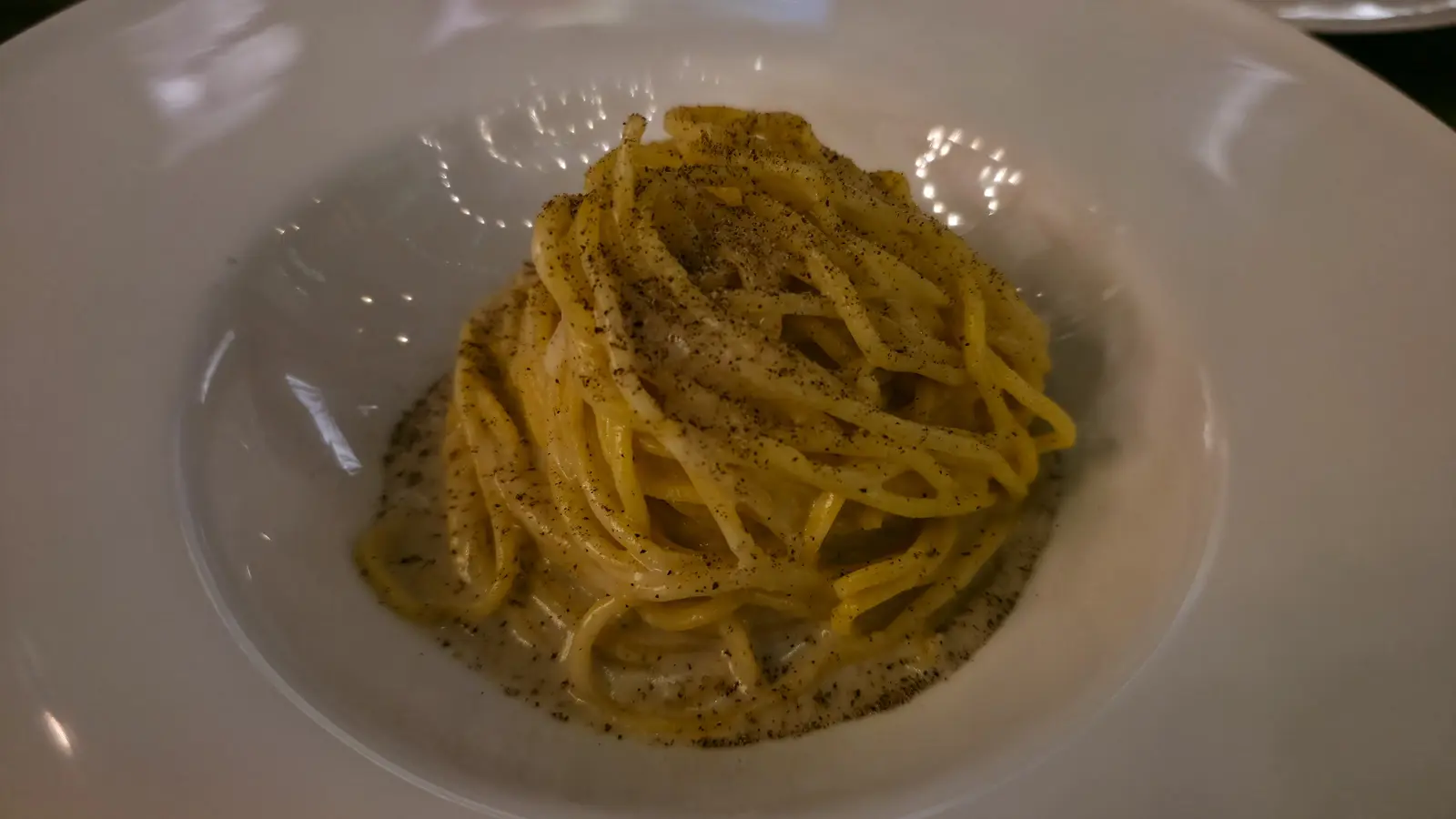 Linguine cacio e pepe coated in a pale cheese sauce and black pepper in a wide white bowl at The Duchess, Amsterdam