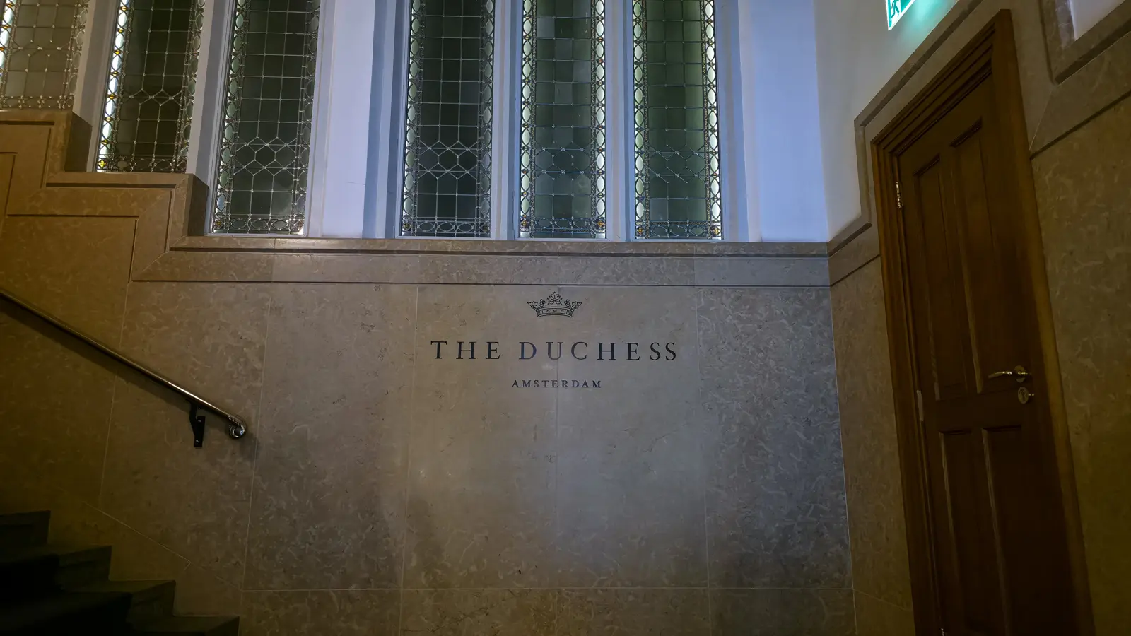 The Duchess name and crown logo on a stone wall beside the staircase, under tall leaded-glass windows