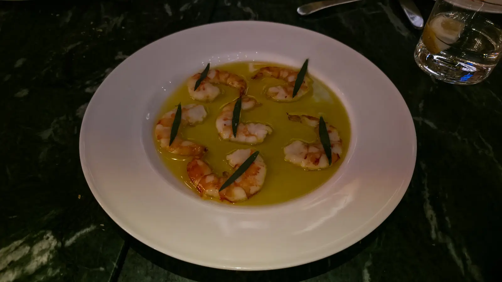 Prawns in a shallow pool of olive oil, each topped with a green leaf, in a wide white bowl at The Duchess, Amsterdam