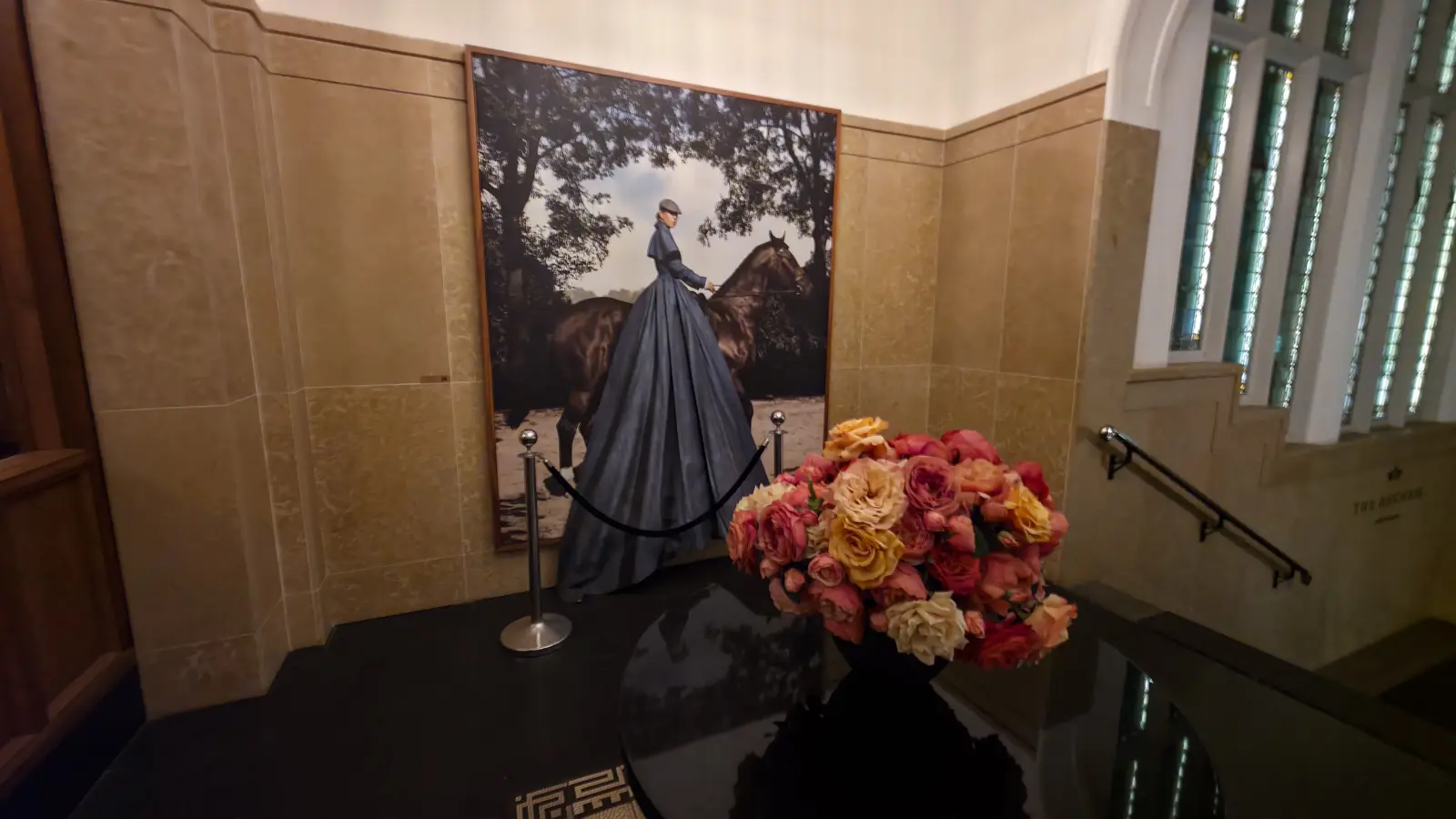 A large photograph of a rider in a grey gown on a dark horse, roped off beside the stairs, with a bowl of roses in front, at The Duchess
