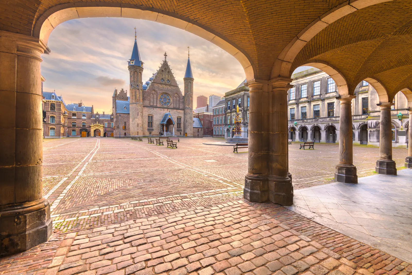 The Ridderzaal in the Binnenhof, The Hague, framed through a stone arcade across an empty cobbled square at dusk