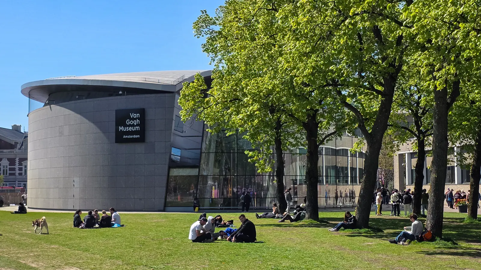People picnicking on the lawn beside the curved grey Kurokawa wing of the Van Gogh Museum on Museumplein