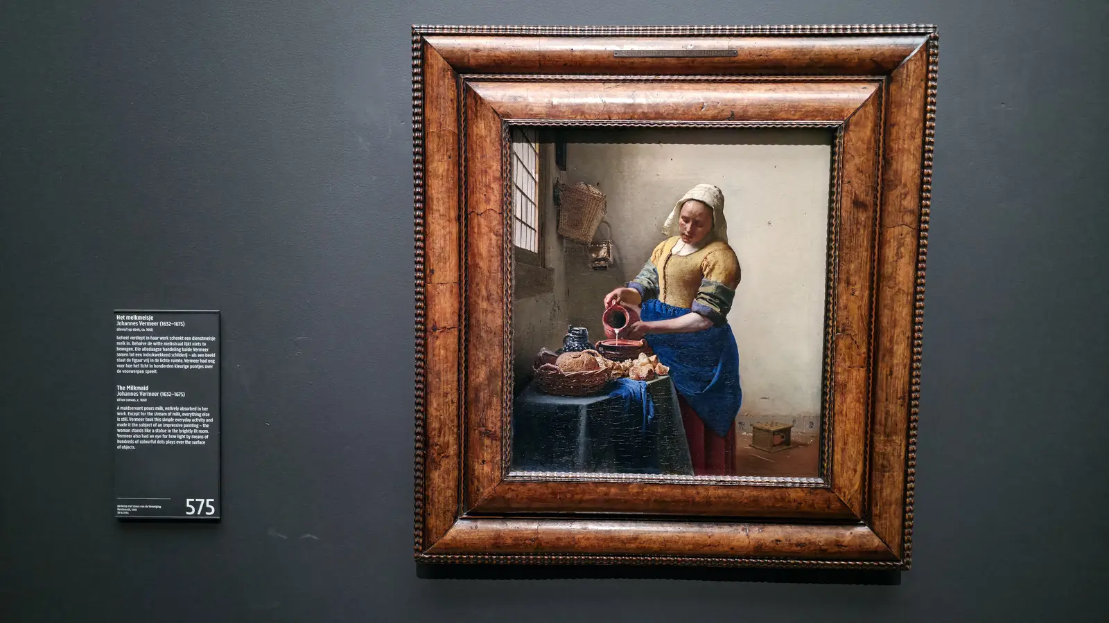 Vermeer's The Milkmaid in its frame at the Rijksmuseum, a maid in yellow and blue pouring milk beside a window