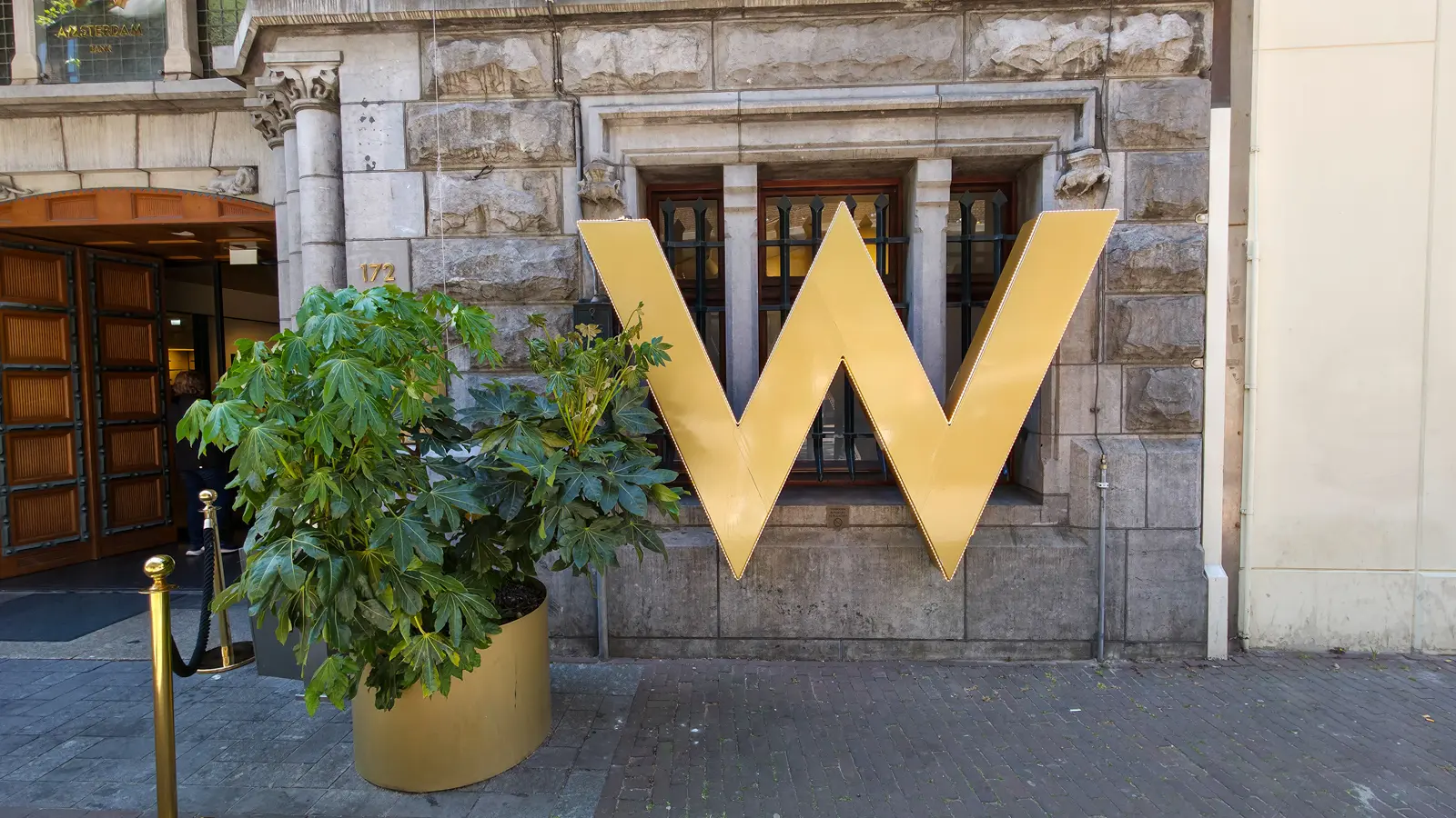 The gold W sign outside the W Amsterdam at Spuistraat 172, beside the wooden entrance doors and a gold planter