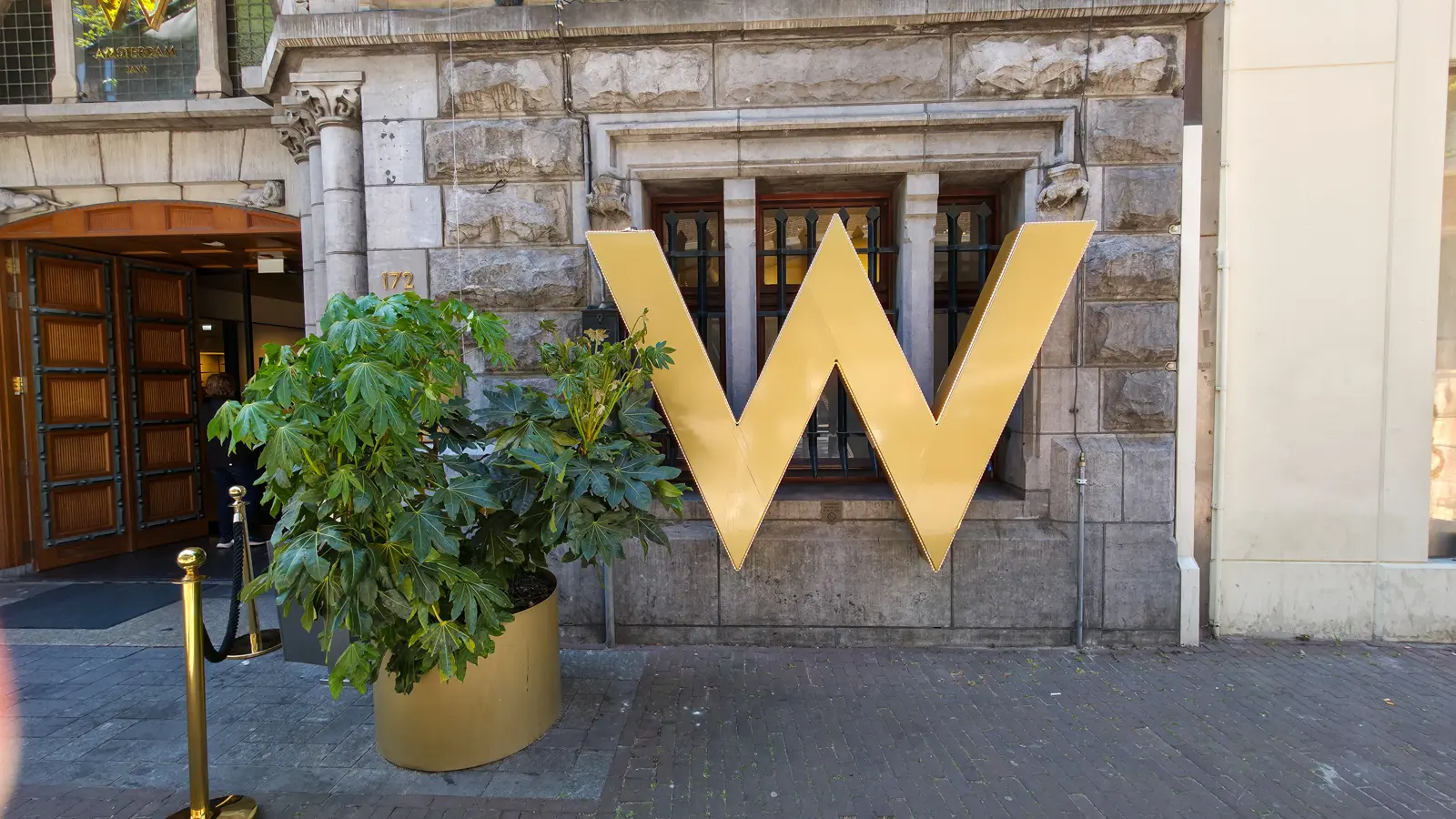 The gold W sign outside the W Amsterdam at Spuistraat 172, beside the wooden entrance doors and a gold planter