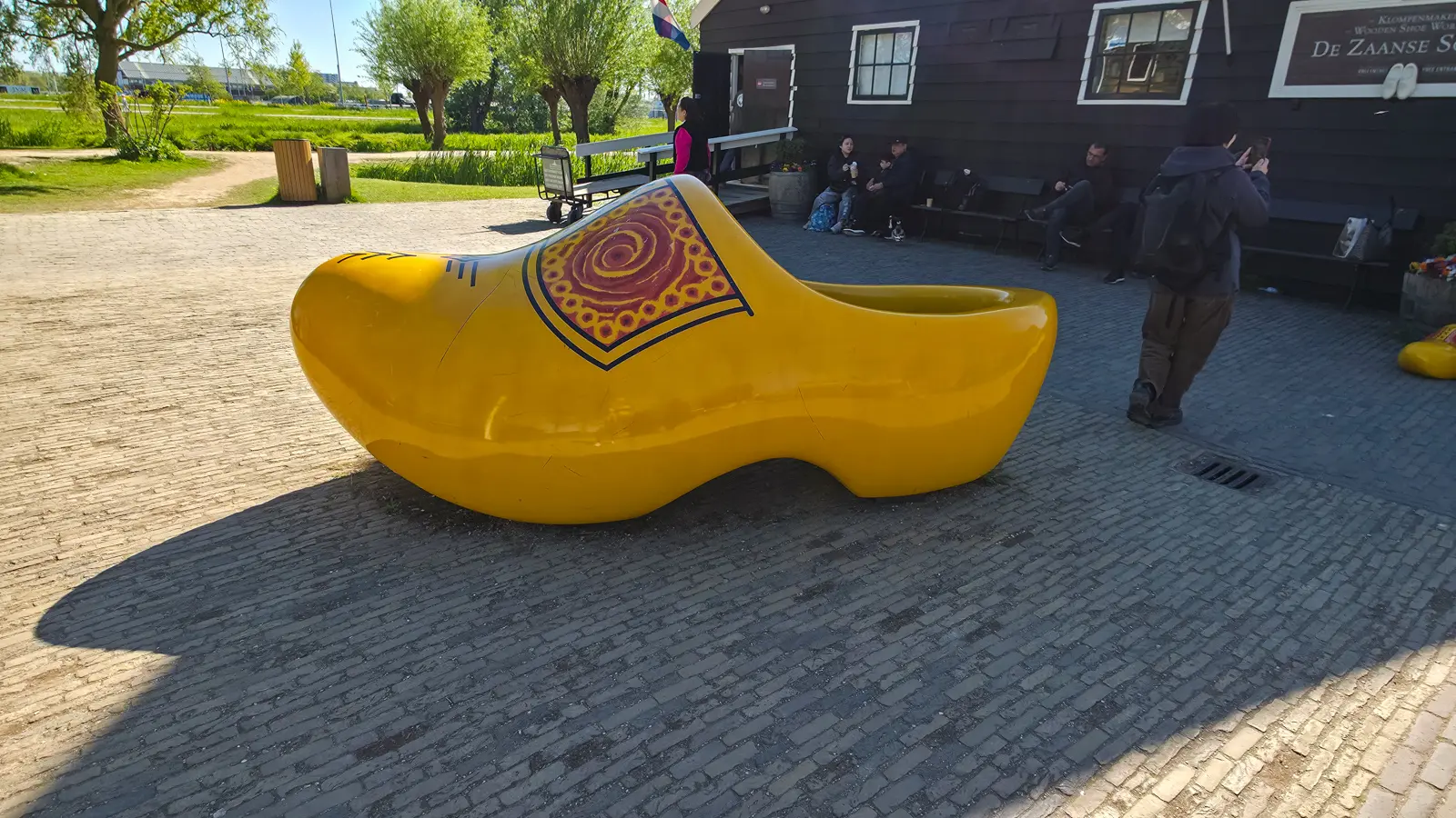 A giant yellow clog painted with a red swirl outside the clog workshop at Zaanse Schans, with visitors on benches behind